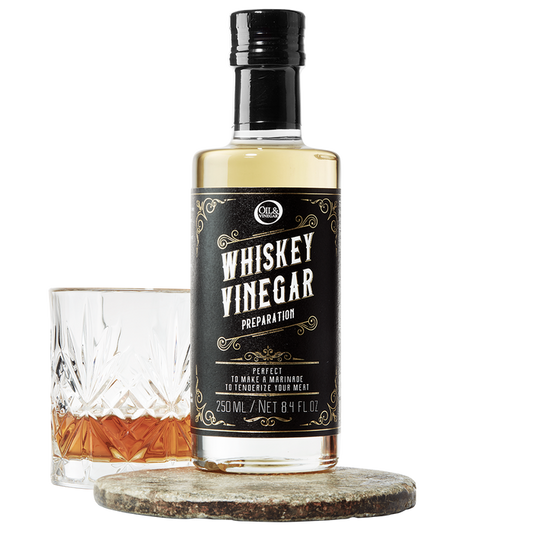 A bottle of whiskey vinegar with a label that reads 'WHISKEY VINEGAR', accompanied by a glass filled with a amber-colored liquid.