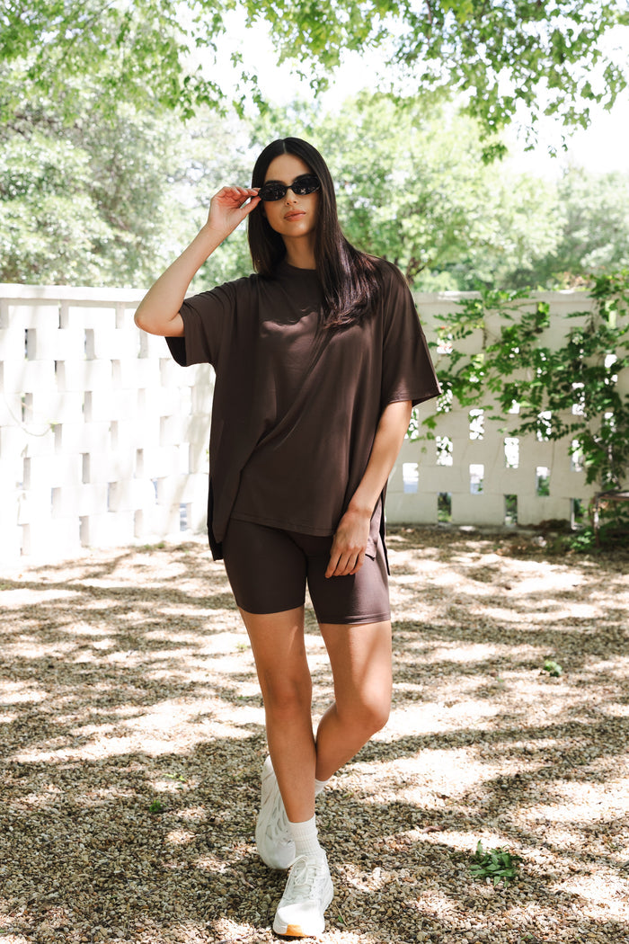 Female posing outside in front of a white fence wearing the Women’s Biker Short Set in Espresso