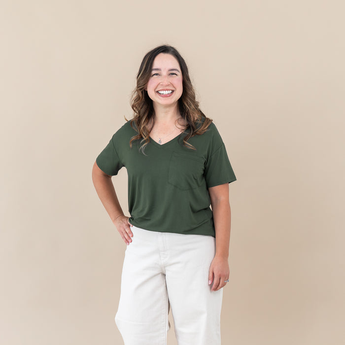 Woman wearing Women’s Relaxed Fit V-Neck in Fir and white pants against a beige background